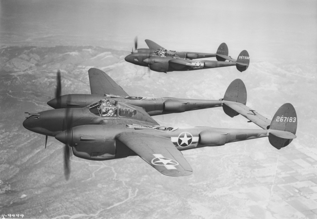 The image shows three vintage military aircraft flying in formation with twin tail booms and a single pilot in each cockpit over a landscape.